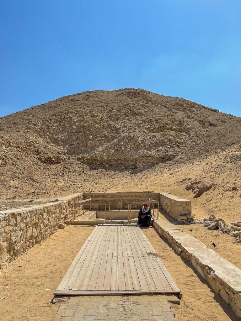 A man sits in front of the entrance to the pyramid of Teti